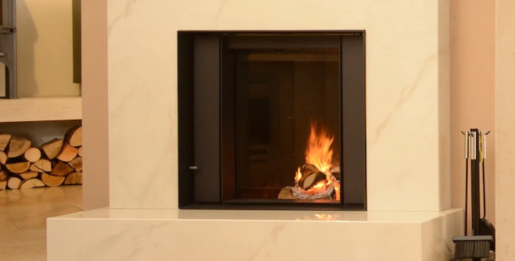 A minimalist sintered stone hearth with a sleek black firebox and visible flames, designed in a modern living space with natural elements like stacked firewood.