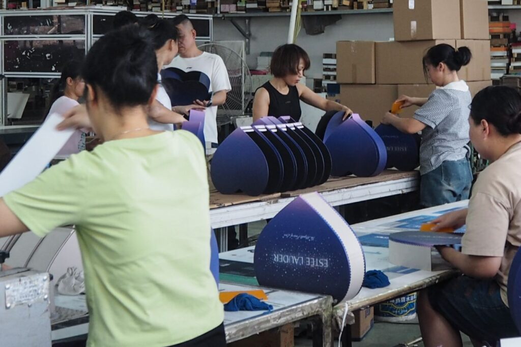 Team of workers assembling heart-shaped custom packaging boxes in a production line.