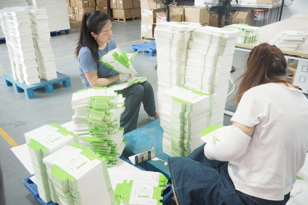 Workers inspecting and stacking packaging boxes for quality assurance.