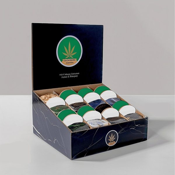 Open cardboard display box with a navy-blue exterior featuring a marijuana leaf logo, holding multiple circular containers.