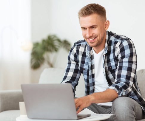 happy-man-using-laptop-sitting-on-couch-JTR57HD.jpg